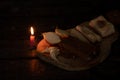 a piece of bacon, onion, garlic, black bread on a wooden table in the dark next to a burning candle, candlelight dinner