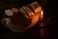 a piece of bacon, onion, garlic, black bread on a wooden table in the dark next to a burning candle, candlelight dinner