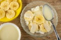 Banana in saucer, bowl with condensed milk, spoon in bowl with cottage cheese, slices of banana and condensed milk on table. Top Royalty Free Stock Photo