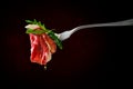 Piece of beef carpaccio on fork with dripping olive oil over black background
