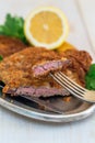 Piece of beef schnitzel on a fork, lemon and parsley.