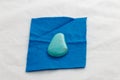 Piece of blue felt with oval turquoise bead for embroidery on white background. Handcraft, process of making of bijouterie