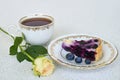 Piece of blueberry pie on a plate, cup of tea and white rose on a white background - close up Royalty Free Stock Photo