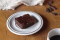 Piece of brownie on a white plate on wooden table.