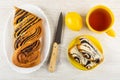 Piece of bun in dish, knife, lemon, slices of bun with poppy in saucer, cup of tea on wooden table. Top view