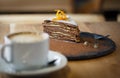Piece of cacao sliced cake on a slate round plate with a cup of capuchino