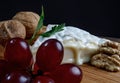 A piece of camembert cheese with nuts and grapes lie on a wooden board. Camembert cheese with white noble mold Royalty Free Stock Photo