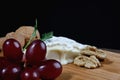 A piece of camembert cheese with nuts and grapes lie on a wooden board. Camembert cheese with white noble mold Royalty Free Stock Photo