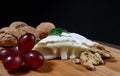 A piece of camembert cheese with nuts and grapes lie on a wooden board. Camembert cheese with white noble mold Royalty Free Stock Photo
