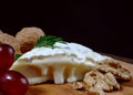 A piece of camembert cheese with nuts and grapes lie on a wooden board. Camembert cheese with white noble mold Royalty Free Stock Photo