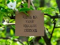 Piece of cardboard with the words What Is Your Excuse Today? on it hanging on a pear tree branch with blossoms and leaves using a