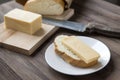 Piece of cheese on bread on a white plate, loaf, knife, wooden background, sandwich Royalty Free Stock Photo
