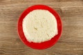 Piece of cheese in polyethylene pack on red saucer on wooden table. Top view