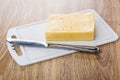 Piece of cheese, table knife on plastic cutting board