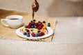 Piece of cheesecake decorated with raspberry, blueberry berries with chocolate falls on table with a cup of coffee