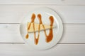 A piece of cheesecake, drizzled in caramel sauce on a white plate standing on wooden white table. The view from the top