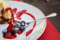 Piece of cheesecake with spoon on white plate with blueberry and jam