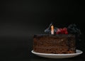 Piece of chocolate birthday cake with one extinguished candle on white plate on deep black background. Birthday party Royalty Free Stock Photo