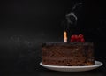 Piece of chocolate birthday cake with one extinguished candle on white plate on deep black background. Birthday party Royalty Free Stock Photo