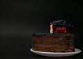 Piece of chocolate birthday cake with one extinguished candle on white plate on deep black background. Birthday party Royalty Free Stock Photo