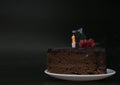 Piece of chocolate birthday cake with one extinguished candle on white plate on deep black background. Birthday party Royalty Free Stock Photo