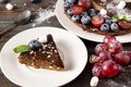 Piece of chocolate cake with fresh berries, blueberries, grapes, powdered sugar and mint on a white plate on a wooden Royalty Free Stock Photo