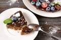 Piece of chocolate cake with fresh berries, blueberries, grapes, powdered sugar and mint on a white plate on a wooden,  spoon Royalty Free Stock Photo