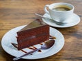 Piece of chocolate cake with spoon on white plate. Cup of coffee on background