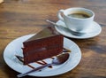 Piece of chocolate cake with spoon on white plate. Cup of coffee on background