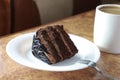 Piece of chocolate cake on a white plate close-up. next to a fork and a cup of coffee. horizontal Royalty Free Stock Photo