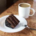 Piece of chocolate cake on a white plate close-up. next to a fork and a cup of coffee. horizontal Royalty Free Stock Photo