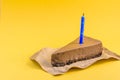 A piece of Chocolate cheesecake with blue candle on a yellow background