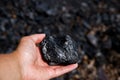 Piece of coal in hand on the background of black coal. Selective focus Royalty Free Stock Photo