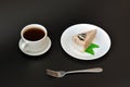 A piece of cream cheesecake with mint on a plate, a cup of hot black coffee and a fork on a black background Royalty Free Stock Photo