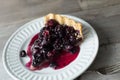 Piece of dark berry pie on a small white dessert plate on a rustic table. Copy space.