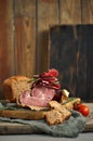 A piece of delectable ham paired with basil leaves, ripe tomatoes, and fresh bread elegantly arranged on a rustic wooden platter.