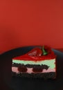 a piece of delicious sweet beautiful bright cake with strawberries on a black kitchen plate and a red background Royalty Free Stock Photo