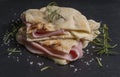 A piece of focaccia is garnished with slices of cheese and ham, decorated with sprigs of rosemary and coarse salt, on a slate base Royalty Free Stock Photo