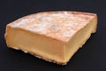 Piece of French Saint-Nectaire farmer`s cheese close-up on a black background