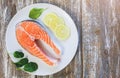 A piece of fresh salmon fish steak on a white plate with spinach and lemon, on  a gray wooden background. Omega 3 vitamin, healthy Royalty Free Stock Photo