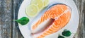 A piece of fresh salmon fish steak on a white plate with spinach and lemon, on  a gray wooden background. Omega 3 vitamin, healthy Royalty Free Stock Photo