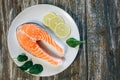 A piece of fresh salmon fish steak on a white plate with spinach and lemon, on  a gray wooden background. Omega 3 vitamin, healthy Royalty Free Stock Photo