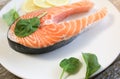 A piece of fresh salmon fish steak on a white plate with spinach and lemon, on  a gray wooden background. Omega 3 vitamin, healthy Royalty Free Stock Photo