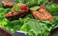 A piece of fried fish fillett served on blue glass table with lettuce, lime, tomato and herbs