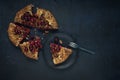 A piece of galette with ripe red cherry filling with dessert fork on black plate. Homemade sweet open pie on dark textured