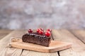 A piece of gluten-free cake in chocolate, decorated with cranberries, on the kitchen board, on a blurry background. Royalty Free Stock Photo