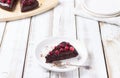 A piece of gluten-free cake in chocolate, decorated with cranberries, on a white plate, on a light wooden background. Royalty Free Stock Photo