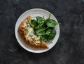 A piece of gorgonzola, pear, honey pizza and fresh spinach in a plate on a dark background, top view