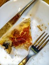 A piece of half-eaten pizza lays on a white plate next to fork and knife, top view. Royalty Free Stock Photo