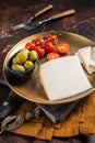 Piece of hard goat cheese in a plate with olives and tomato. Dark background. Top view Royalty Free Stock Photo
